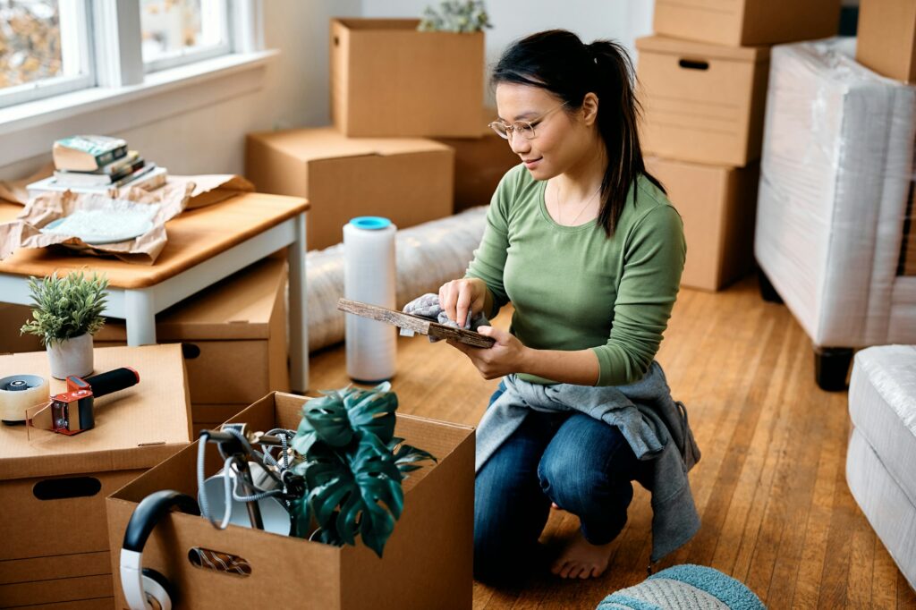 Young Asian woman cleaning photo frame while unpacking her belongings and moving in a new home.